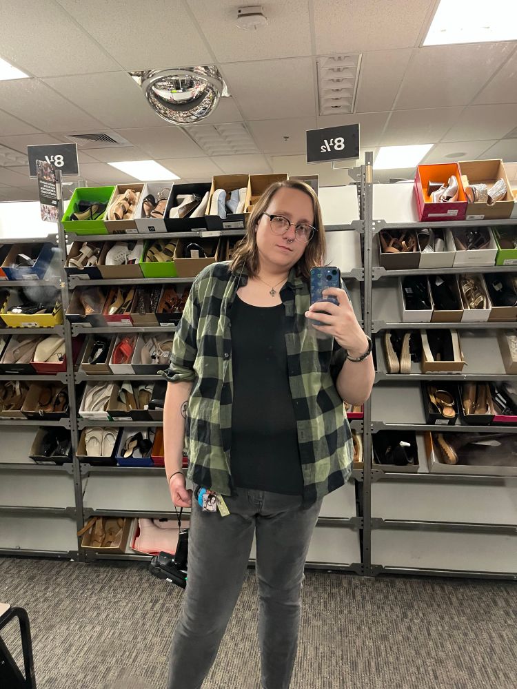 maya taking a mirror selfie in the same shoe isle, revealing she is also wearing fade black jeans and a carabiner with several things hanging from it