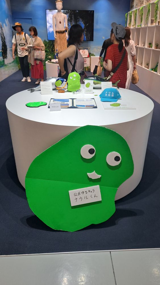 A green blobby mascot shaped like a country 
