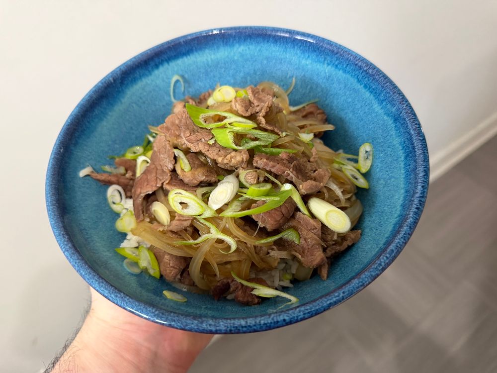 A blue ceramic bowl with beef and onions. Rice is barely visible underneath. 
