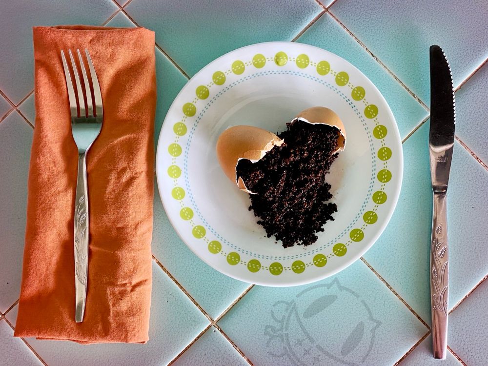 Cracked egg on plate spilling coffee grounds