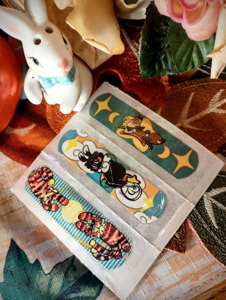 Tiger twin bandaids, shib bandaid and cranberry fox bandaid  on a fall like background and a ceramic bunny accenting the photo