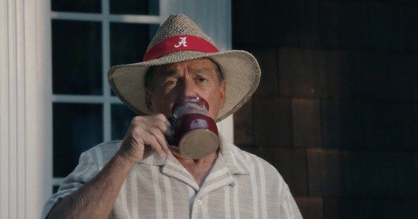 Man with hat with script A looking comfy who is drinking a beverage in a mug, possibly coffee