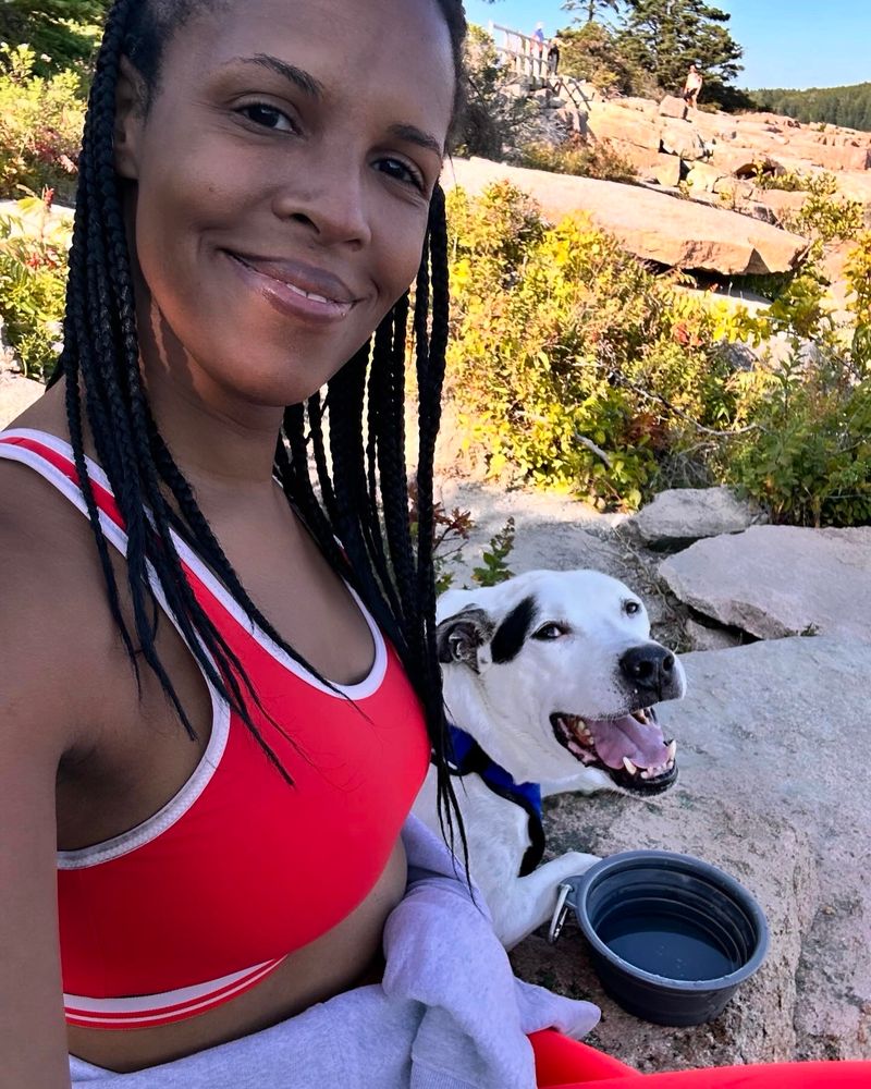 Duke resting with me on a ledge after a hike in Acadia park. He has a bowl of water in front of him and is grinning up at me while I take a selfie.