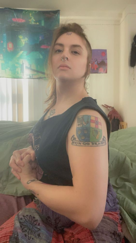 Pretty trans woman showing off her Irish tattoo of a coat of arms of the four historic provinces of Ireland. Ulster, Leinster, Munster, Connaught (in that order and where each is traditionally located on the island.)