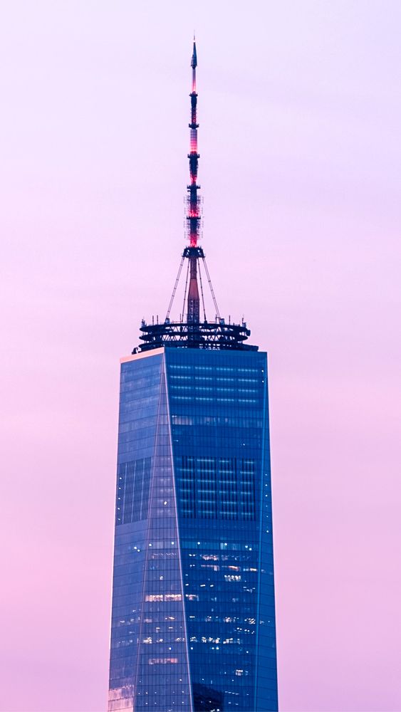 Close up of the top part of One World Trade Center in front of a rosy-hued golden hour sky. 