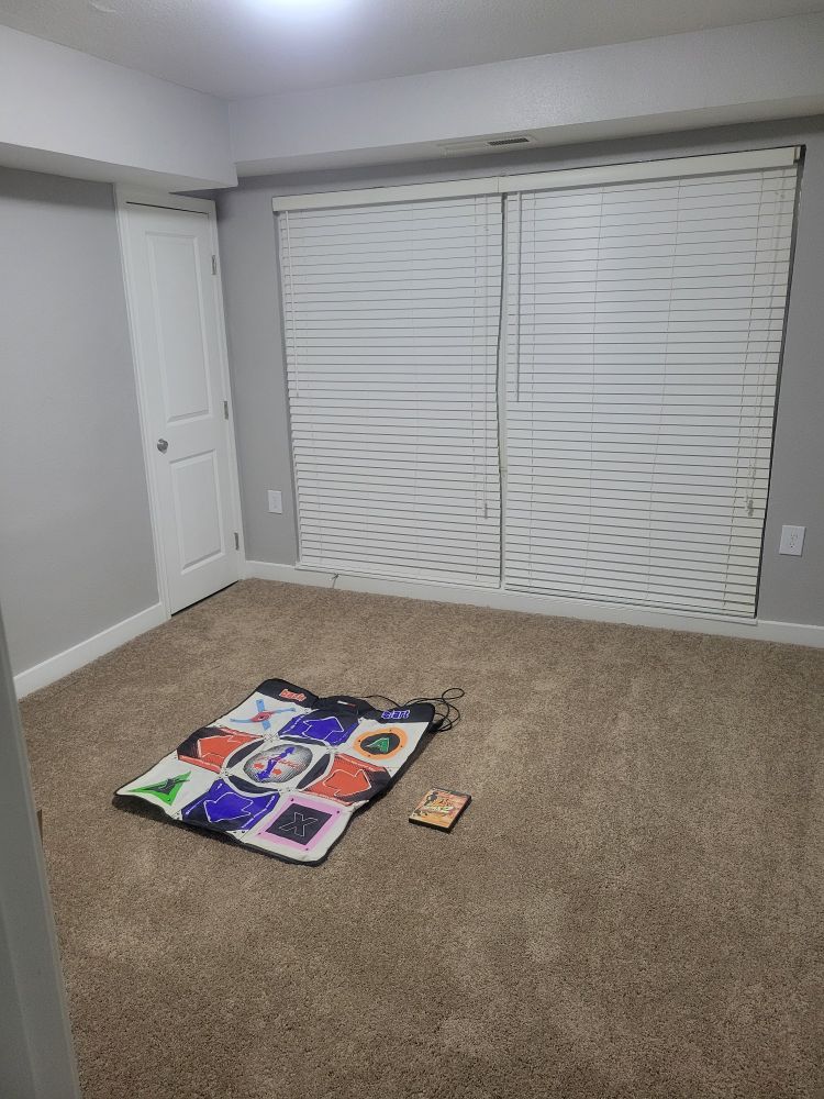 a carpeted bedroom that is completely empty except for a DDR soft dance pad and a copy of DDRMAX2 sitting on the floor