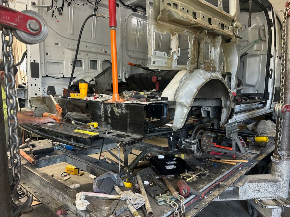 The lower rear of a white van after structural removal, the entire right quarter panel removed, revealing the interior of the van.
