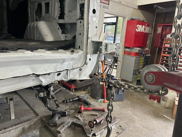 The rear passenger side of a white van, prior to removing its damaged structure, attached to a pulling machine.