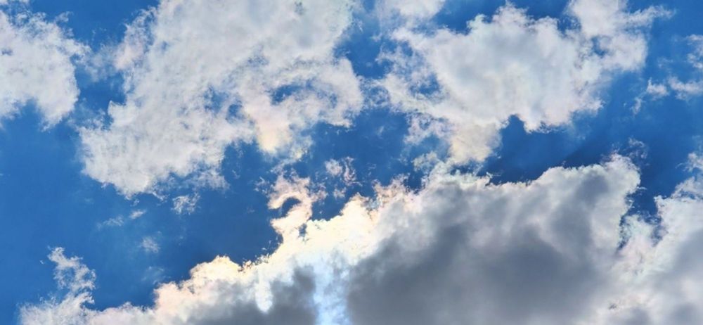 Photo of a blue sky with fluffy white clouds, the sun filtering through