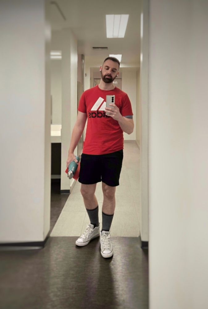 A mirror selfie from the locker room of me in a red Addidas tshirt, black running shorts, dark gray socks and light gray chucks