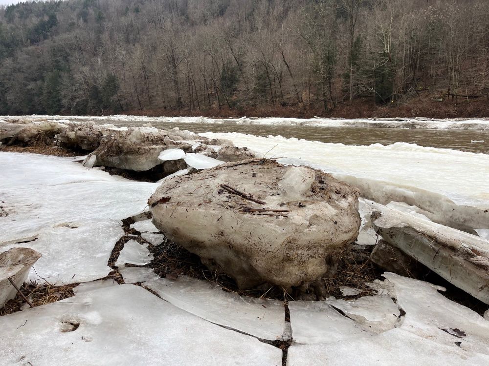 Large ice chunk along river riparian zone sitting on cracked sheet of ice. 