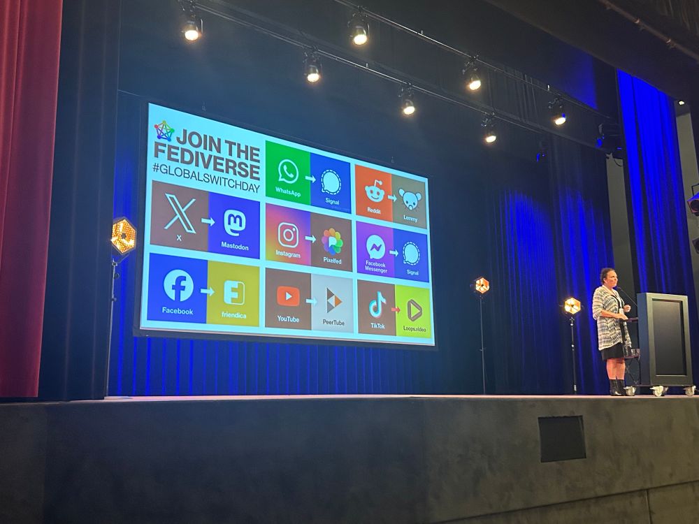Op het podium in Zwolle Marleen Stikker van Waag helemaal rechts. Achter haar op een heel groot scherm de oproep ‘Join the fediverse. Met alle icoontjes van BIG TECH platformen en de icoontjes van de (leukere) alternatieven.
