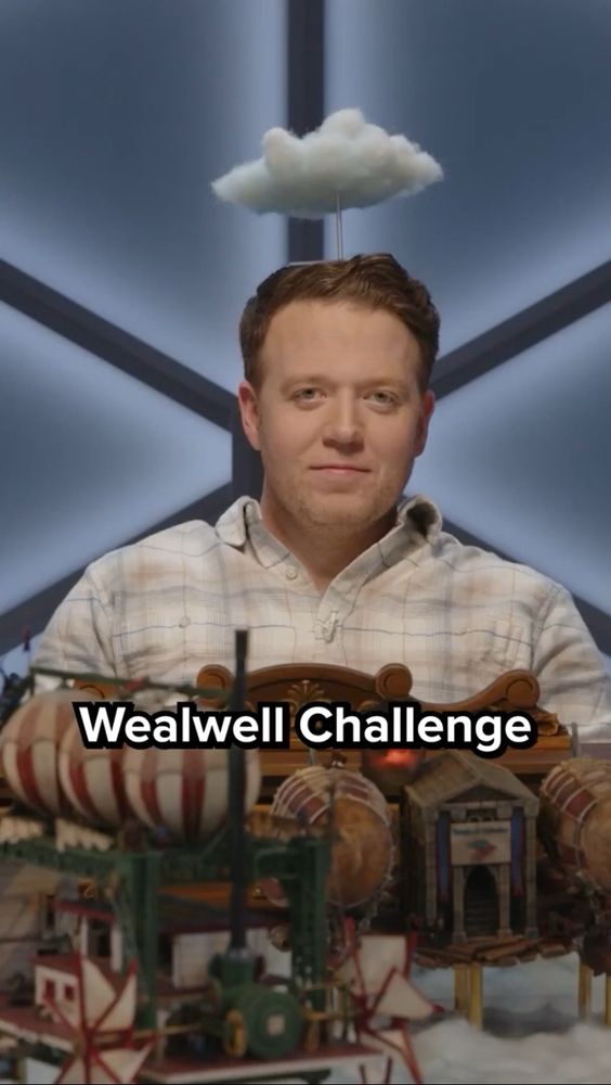 Brennan Lee Mulligan sits behind the GM screen for Dimensions 20: Cloudward, Ho. He balances a cloud prop in his head. The closed captions from Lou (offscreen) reads “Wealwell Challenge.” Brennan has the expression of Kermit the Frog as he looks directly at the camera, for the same reasons that Kermit would look directly at camera.