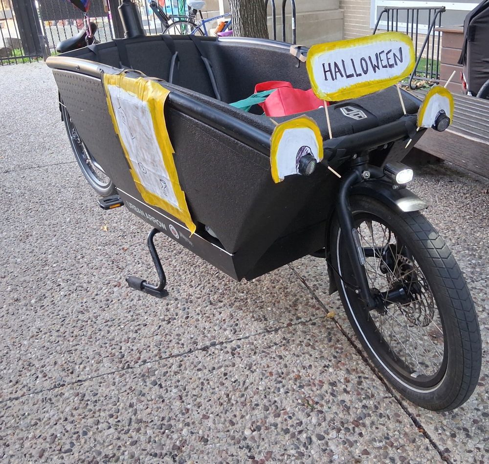Urban Arrow cargo bucket bike with yellow cardboard eyes, windows, and sign attached to make it resemble the Magic School Bus