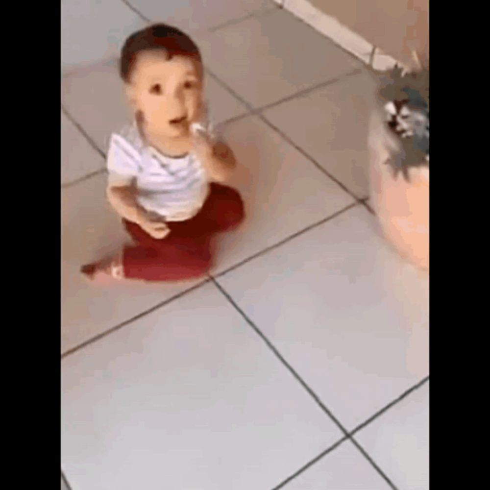 a baby is sitting on a tiled floor eating something .