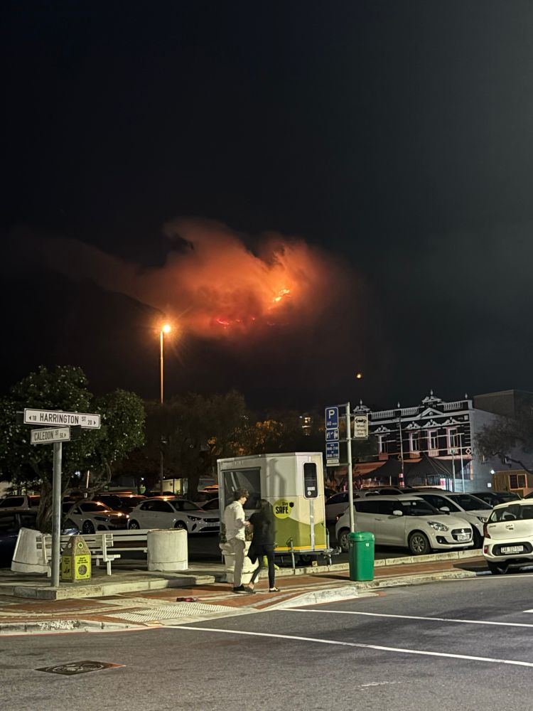 A photograph of a mountain at night. The mountain is invisible in the dark, save for a glowing ring of red fire and smoke. 