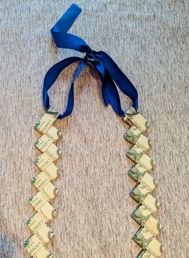 Close up of the top of the lei, 2 strands of the money connected with blue ribbon. 