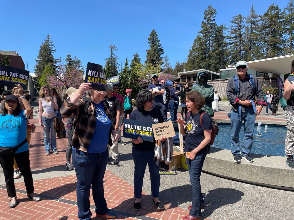 protestors in blue union t-shirts hold up rally signs in front of a fountain