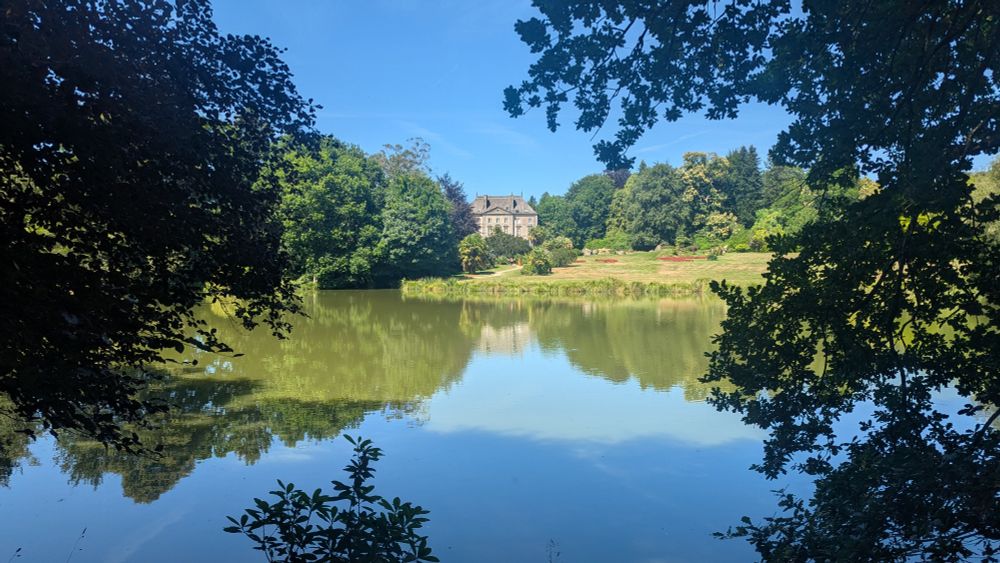 A view of the lake in the foreground and the salon de thé in the background, at "Parc Botanique de Haute Bretagne"