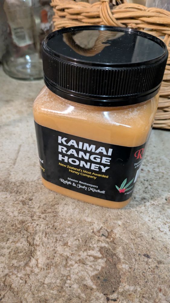 Container of honey, black label reads kaimai range honey.
