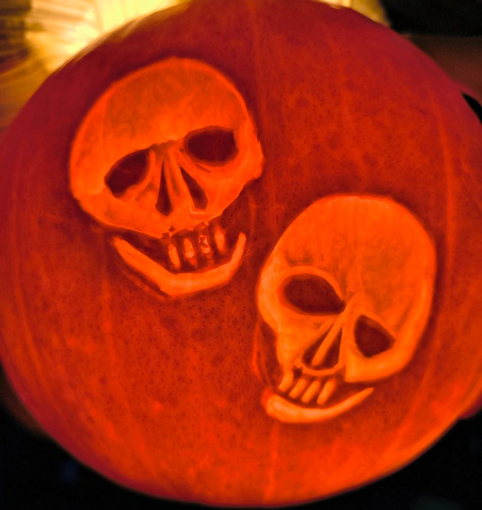 Two skulls carved on a pumpkin, slightly wonky.