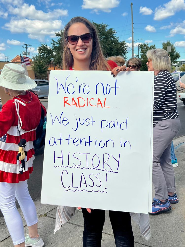 Woman holding a sign: “We’re not radical. We just paid attention in History class.”