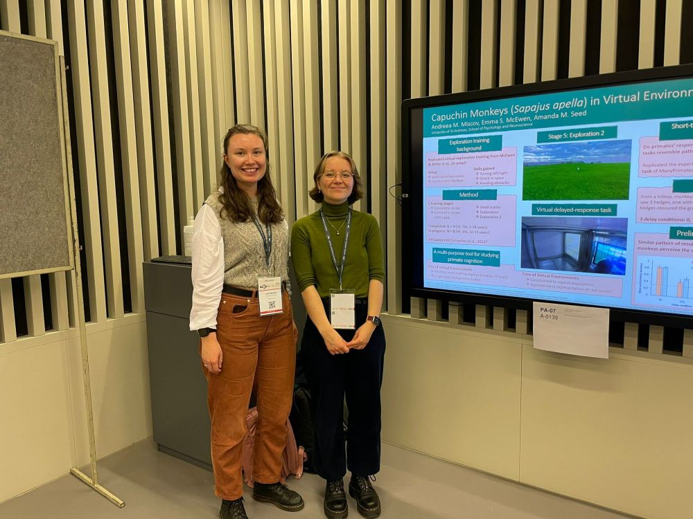 Emma and Andreea standing next to a digital poster presenting work entitled 'Capuchin Monkeys (Sapajus apella) in Virtual Environments'