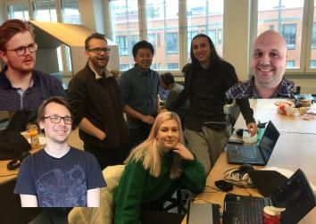 4 game jammers with 3 others cheaply edited in. There is a bright light coming from the window in the background.