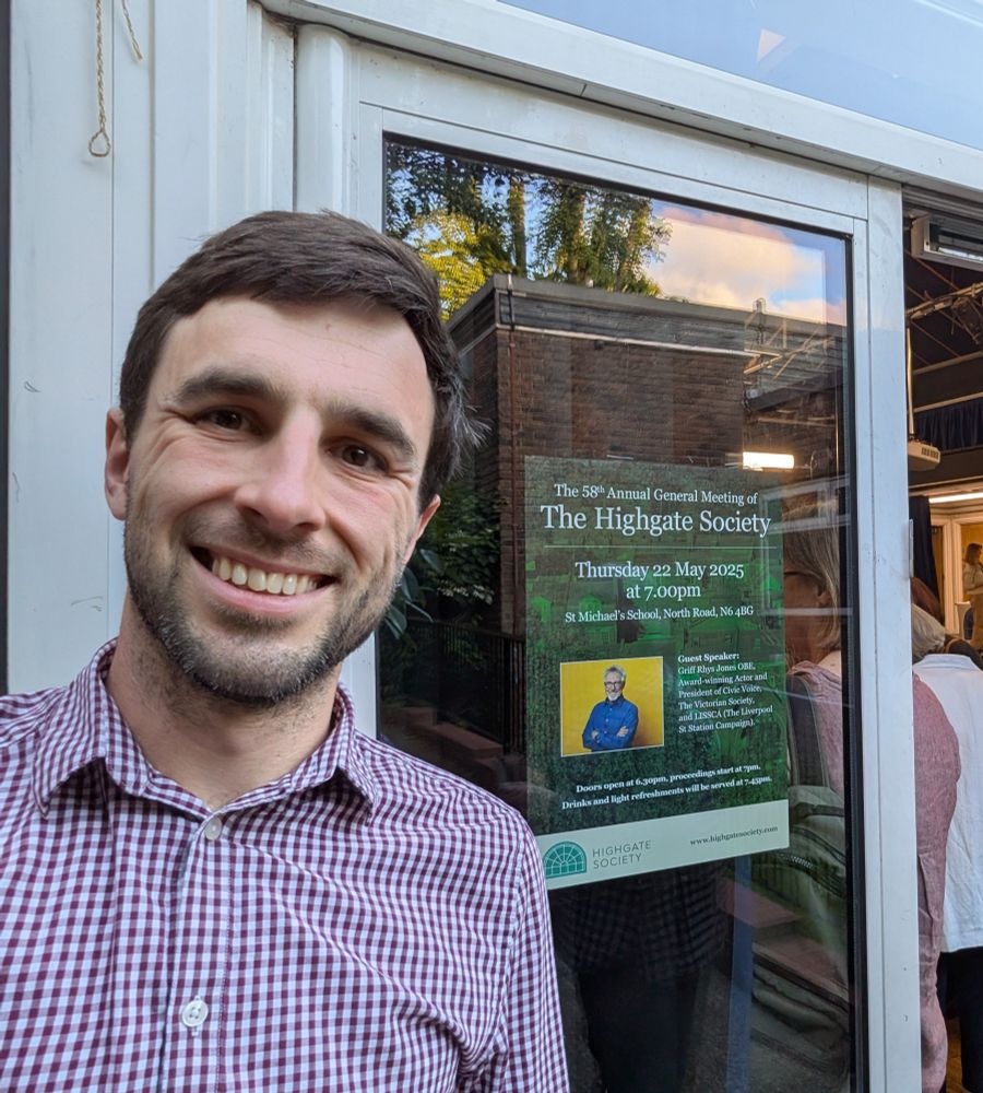 Me, smiling, next to a poster advertising the event inside "Highgate AGM"