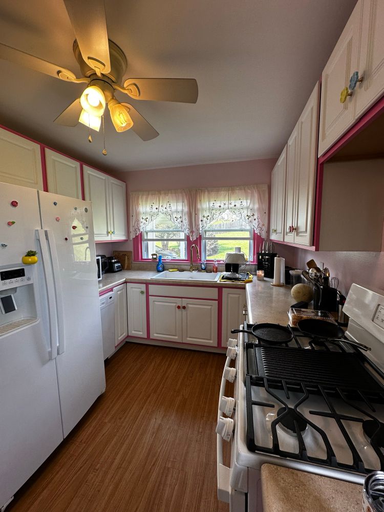 A kitchen with light pink walls and dark pink cabinets with white cabinet doors and flower knobs 