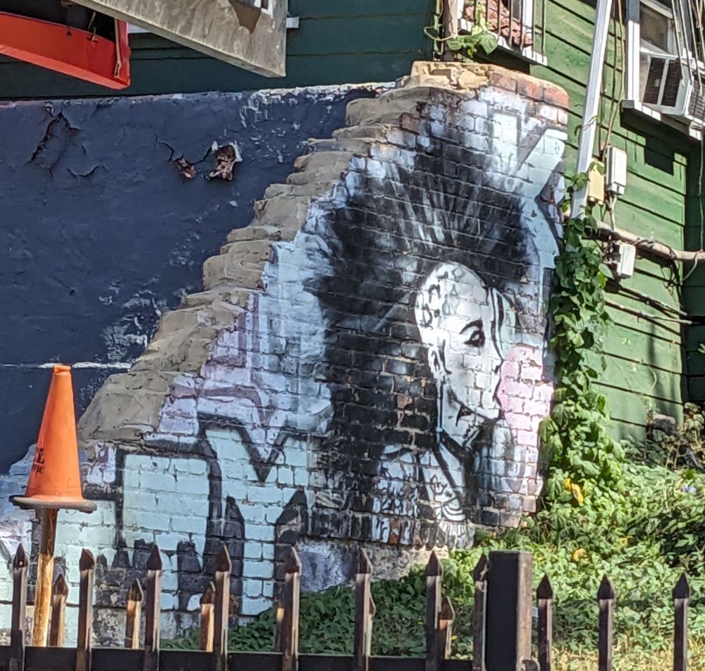 Painting on a wall of a woman with a big mohawk blowing a bubble 