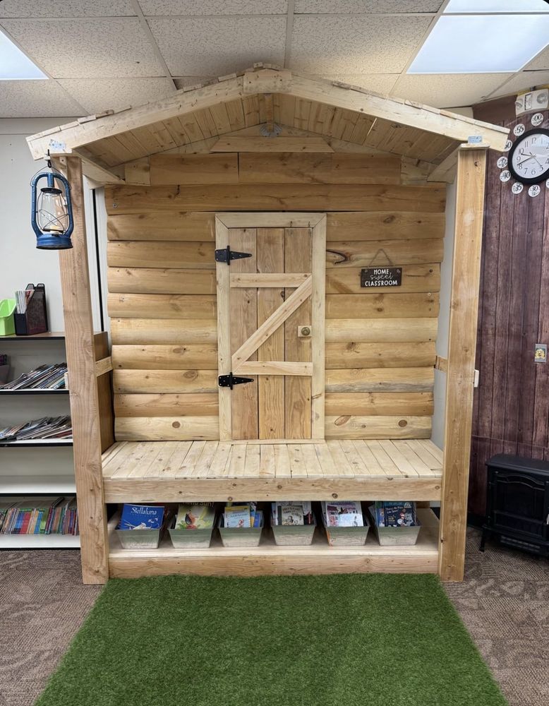 indoor wooden "porch" replica with an overhang, fake door, working lantern, and boxes of school supplies under the porch, in a classroom