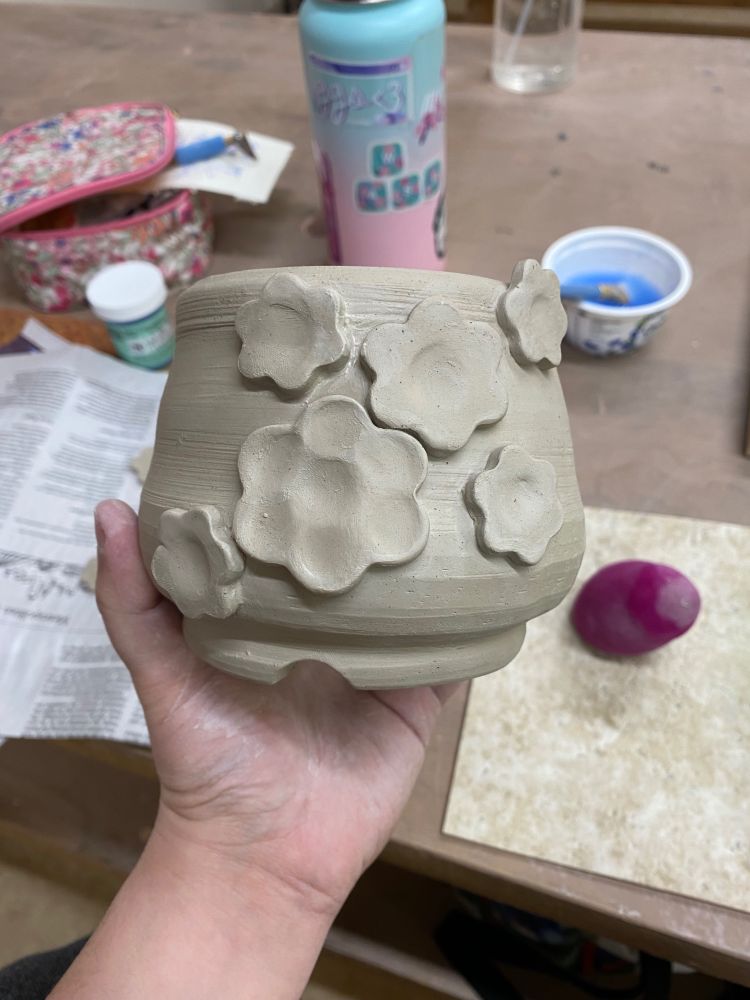 A hand holding a clay pot covered in simple flower shapes. 
