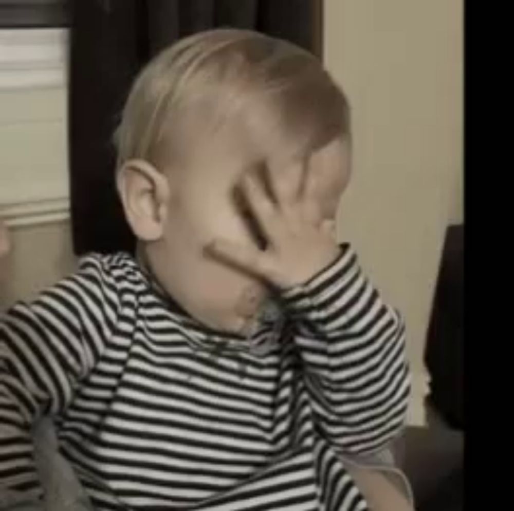 a baby is covering his face with his hand .