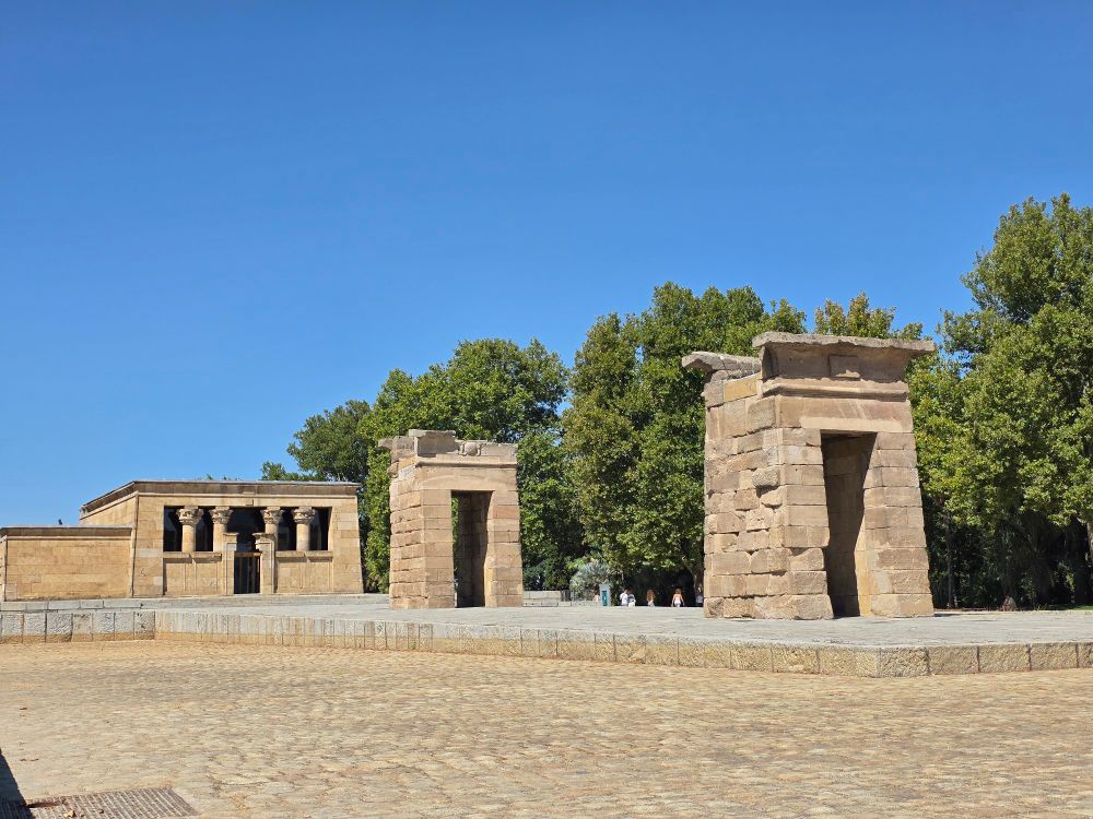 The exterior of the Templo de Debod, which is comprised of a walkway with two arches with stylized keystones and the main mausoleum.