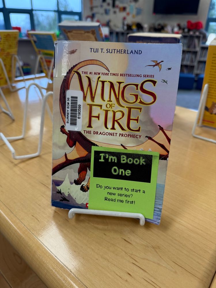 A book on display with a printed post it note that says “I’m Book One”