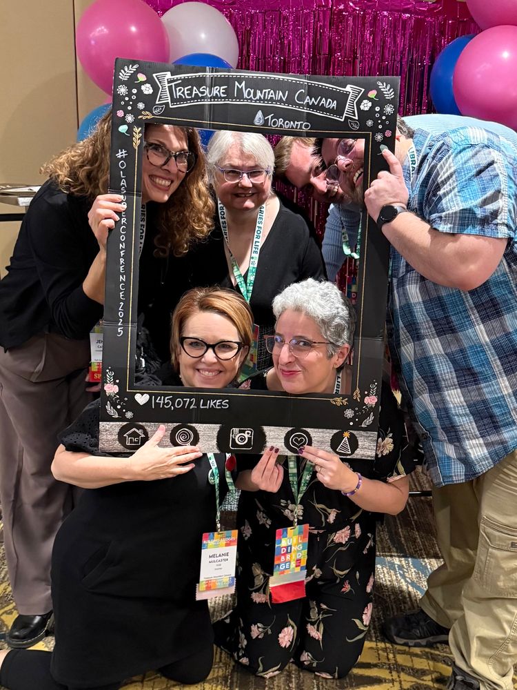 A group photo of the board members of the Canadian School Libraries. They are all fitting into a small cardboard frame that says Treasure Mountain Canada