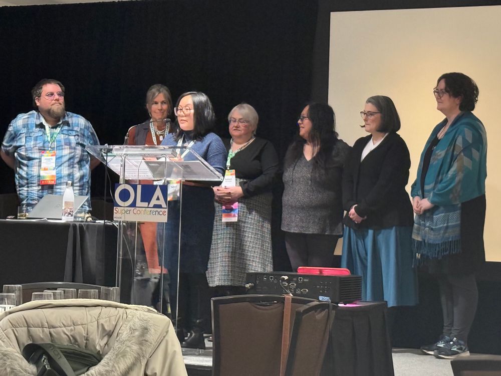 Tammy Le, president of the BCTLA is speaking at a lectern with members of the BCTLA surrounding her. They are accepting an advocacy award as a group