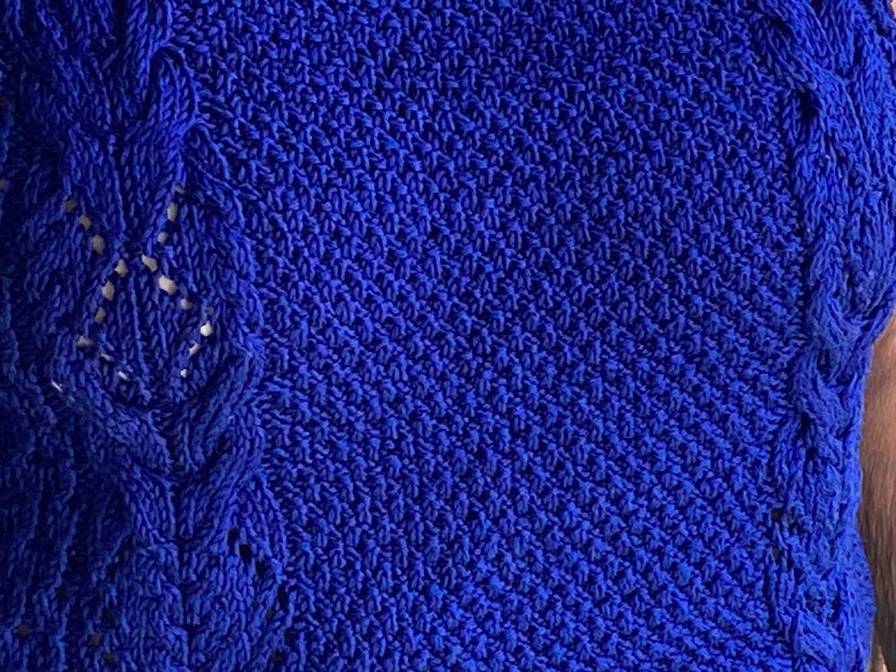 A Bluesky knitted garment with moss stitch and bands of cables on either side. A close up