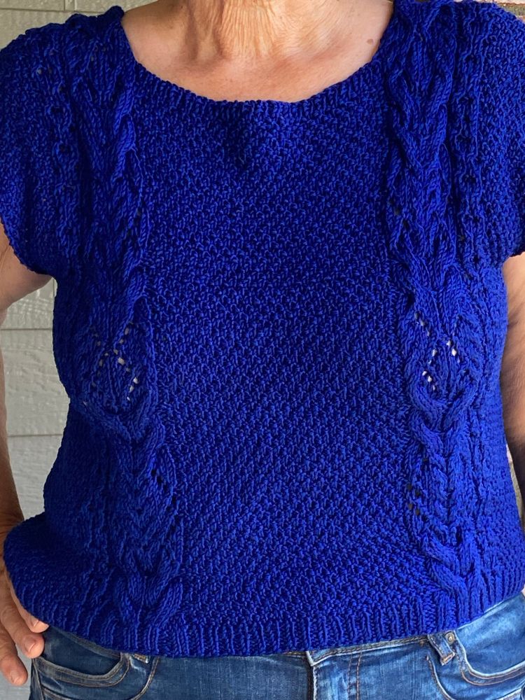 A Bluesky knitted garment with moss stitch and bands of cables on either side. This is the front view. A close up
