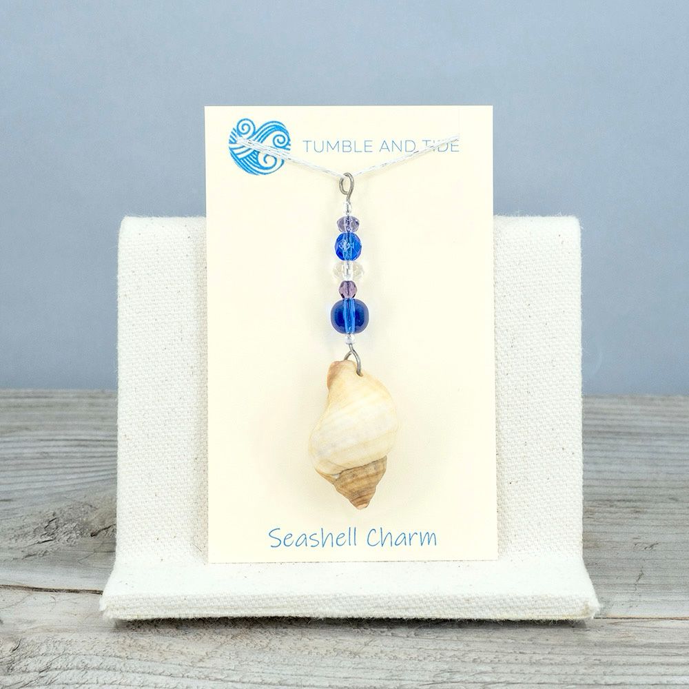 A window charm made from a seashell hanging below a vertical line of colorful glass beads that complement the colors of the shell. The beads are blue, purple, and sparkly clear.