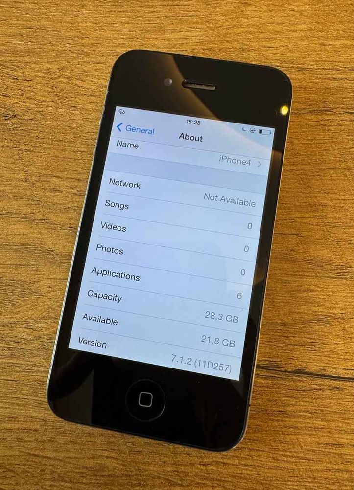 Ein iPhone 4 in schwarz liegt auf einem Holztisch. Es ist ein 32GB Modell.
