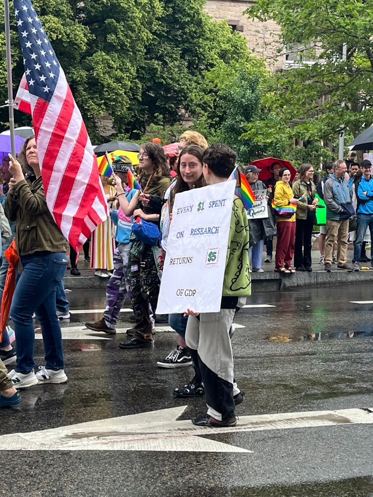 Protester holding sign that says every $1 spent on research returns $5 of gdp 