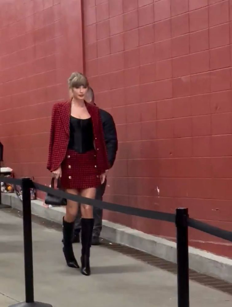 Taylor wearing a red checked blazer and skirt, and black boots (below the knee)