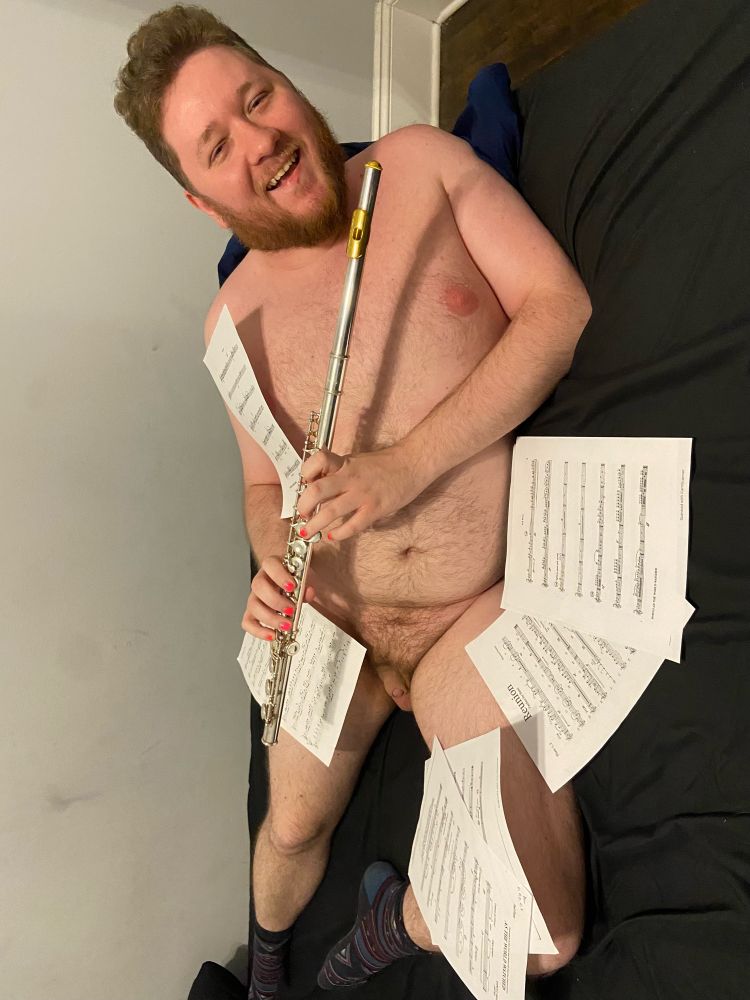 Me, naked and holding a flute on a bed surrounded by sheet music