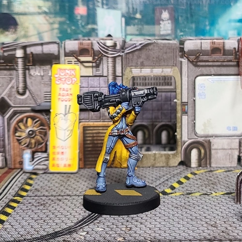 A Cyberpunk Combat Zone Danger Gal miniature painted yellow, blue, brown, tan, and grey. Right side view