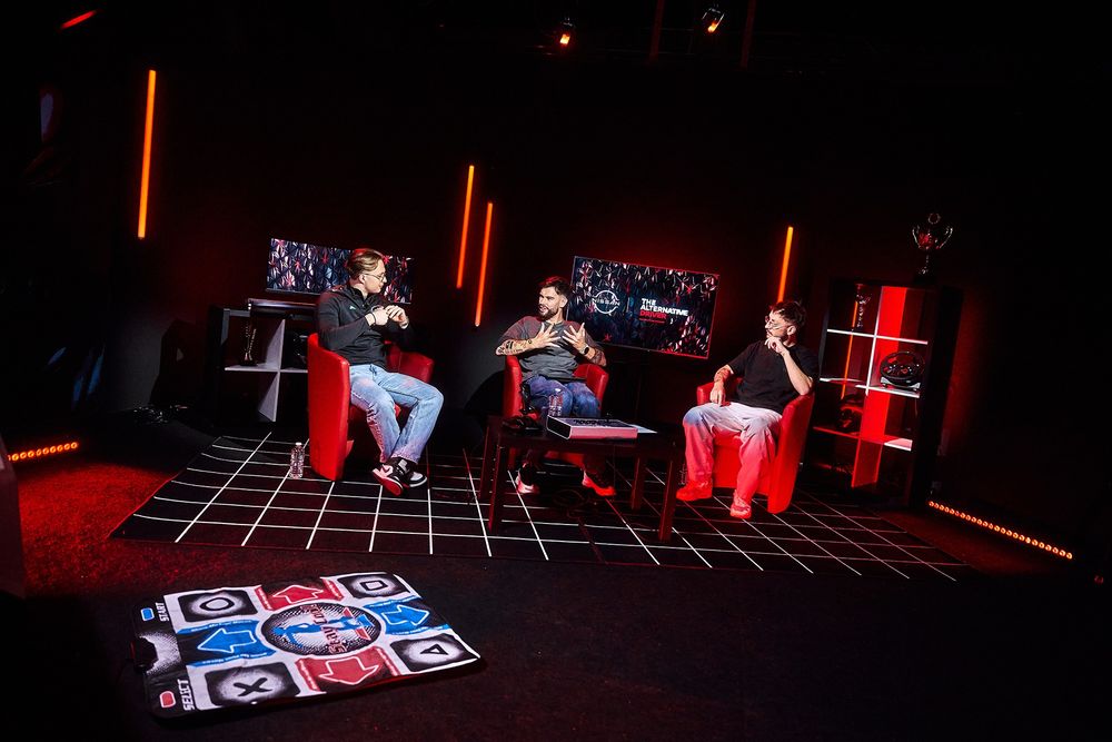 Un deuxième plan large du plateau Gozulting où LeBouseuh, Dobby et Kylian Drumont discutent, assis sur des fauteuils rouges. On peut apercevoir au premier plan un tapis de Dance Dance Revolution.