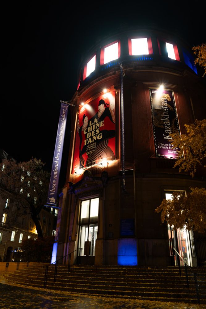 La façade extérieure du Musée Guimet, de nuit. Les illuminations du batiment mettent en valeur les affiches des expositions : la Chine des Tang et le Kazakhstan.