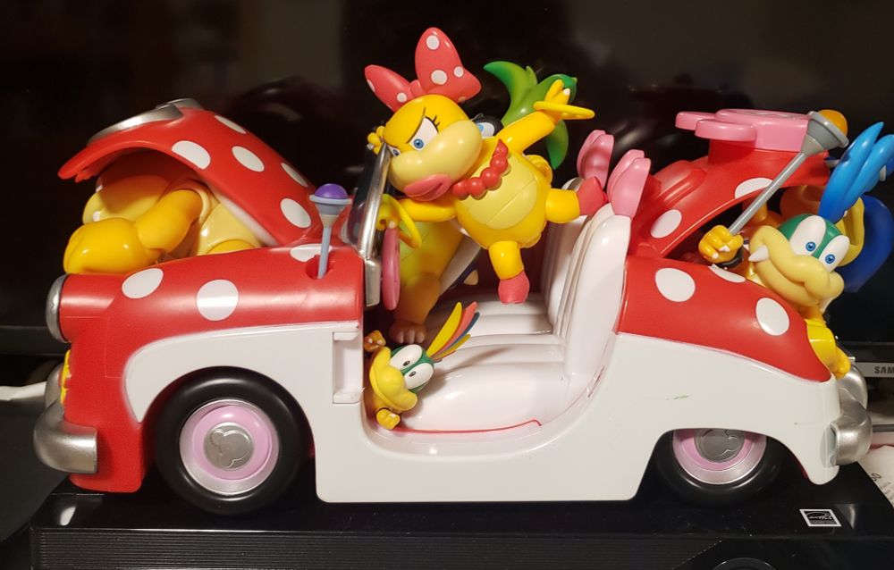 Wendy O. Koopa driving a polka-dotted Minnie Mouse convertible, with Iggy, Lemmy, Larry, Ludwig and Bam Bam along for the ride, either in the passenger seat, the trunk, under the hood, or on the floor.