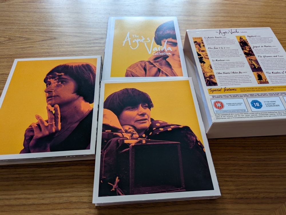Photograph of a blu ray collection of eight Agnes Varda's films. Each of the main sleeves features a photo of Varda at various points of her life with a yellow backdrop